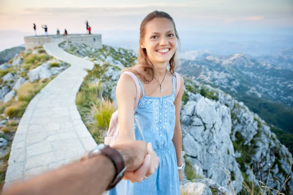 Chica inspirada pasa tiempo con un chico sosteniendo su mano en el fondo de la naturaleza. Jovencita alegre lleva a un amigo a las montañas. Lovcen Montenegro — Foto de Stock