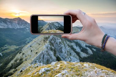 Kadın turist fotoğrafları akıllı telefondan Karadağ 'daki dağ sırasının güzel manzarasını gösteriyor. Seyahat kavramları ve teknoloji. Kapat.