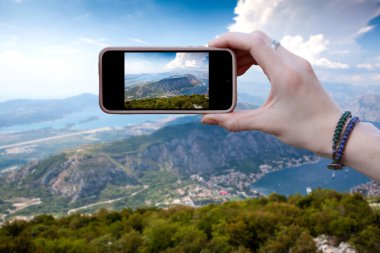 Kadın turist fotoğrafları akıllı telefondan Karadağ 'daki dağ sırasının güzel manzarasını gösteriyor. Seyahat kavramları ve teknoloji. Kapat.