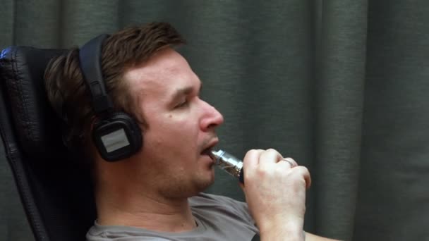 Man listening to music on headphones and smoking an electronic cigarette — Stock Video