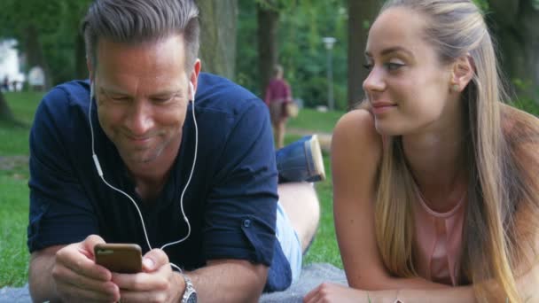 Fin de semana - un par de relajarse en el parque y escuchar música en los auriculares — Vídeo de stock