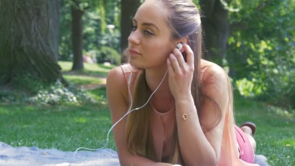 Hermosa joven con auriculares relajándose en el parque y escuchando la música — Vídeos de Stock