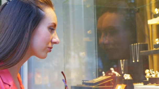 Jovem mulher bonita está olhando para jóias em uma vitrine — Vídeo de Stock