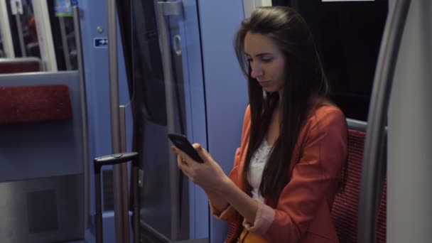 Una joven con un traje que envía mensajes de texto en su teléfono inteligente al regresar a casa en tren — Vídeos de Stock