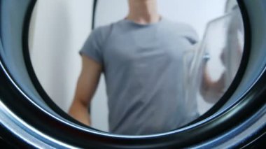 Bir adam çamaşır makinesinin kapısını açar ve içine giysi yüklemek - Içinden görünümü