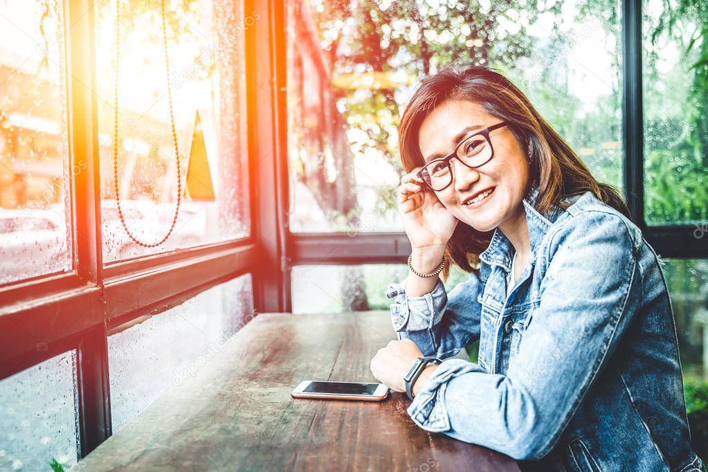 Glasses nerd hipster asian woman sitting smile in glass windows cafe with smartphone