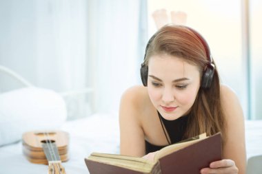 Rahatlamak için kitap okuma ve kulaklıklar müzik dinlemek yatakta yatan kız.