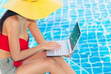 Sevimli Genç Asya kadın kullanarak dizüstü bilgisayar için zevk çalışma içinde yüzme havuz sırasında yaz tatil