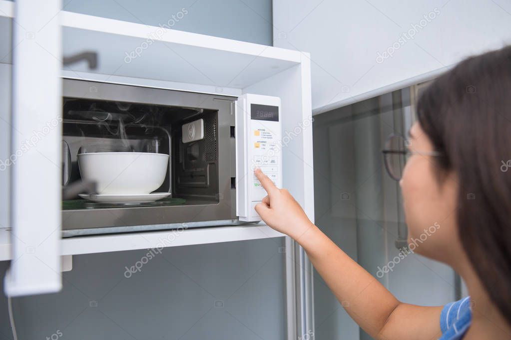 women reheat food by using microwave oven with glass ceramic bowl.