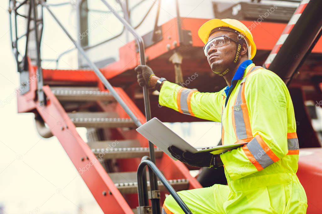 Black African Staff foreman intend to work loading worker using laptop computer to control cargo shipping in logistic warehouse.