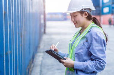 Lojistik kargo yükleme alanında çalışan kadın personel, ithalat konteynır kodunun gümrük detaylarını kontrol etmek için tablet kablosuz teknolojisini kullanmaktan memnun..