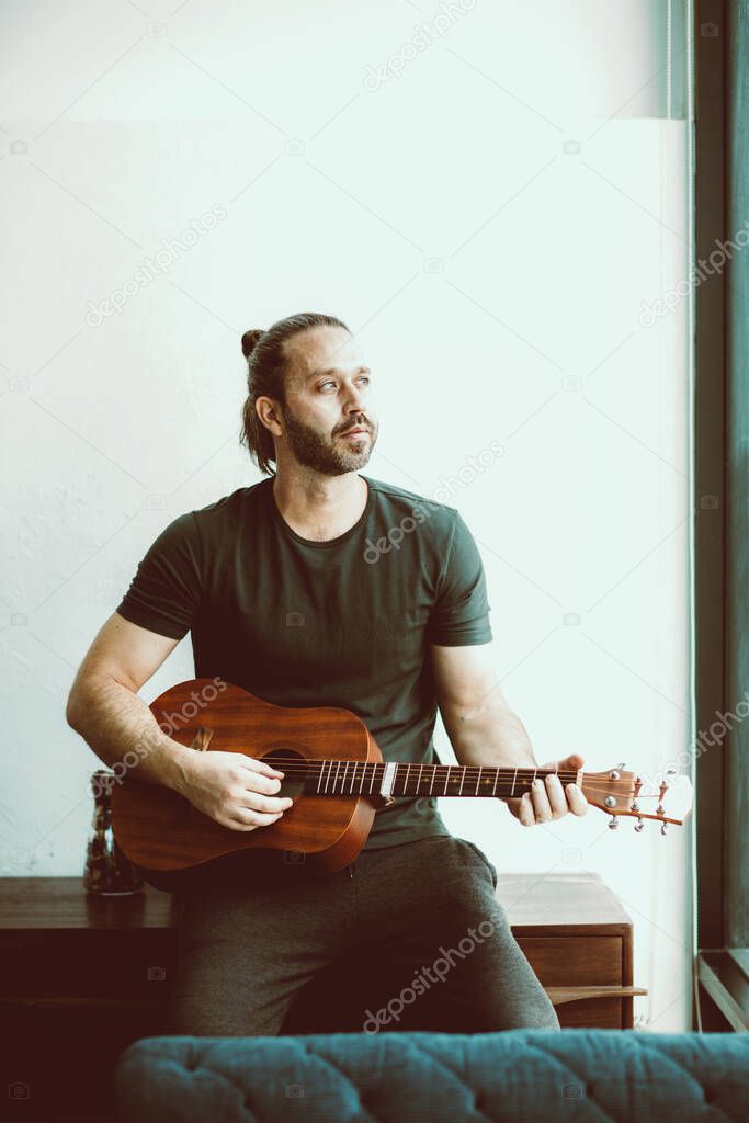 Man playing guitar looking away missing someone single lonely at home vintage color tone vertical shot.