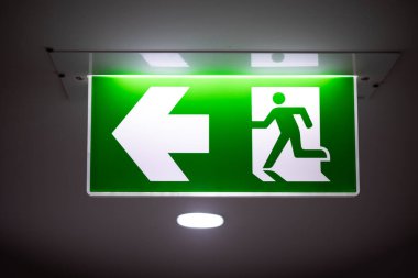 Ok yönünden çıkış yolu, kaçış kılavuzu yeşil ışık çıkış işareti tavan koridorundaki karanlık oda tesisinde acil çıkış işareti.