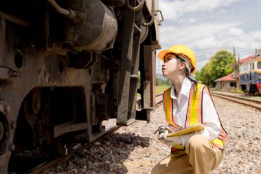 Asyalı genç mühendis tren istasyonunda çalışıyor, eski lokomotif bakım işleri motoru araba lokomotifi bakımı altında.