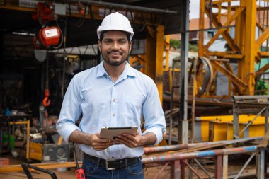 İspanyol asıllı Hintli inşaat mühendisi inşaat alanında güvenlik kaskı ve tablet bilgisayarlı mutlu gülümsemeyle çalışan erkek işçi portresi.
