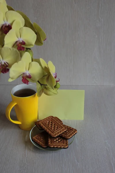 Yellow orchid, mug of tea , cookies and phone on a wooden background