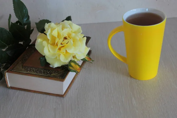 Yellow rose, a book and a mug of tea on the table.