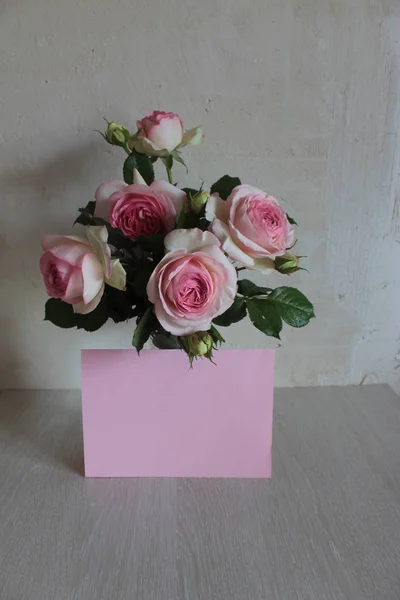 Bouquet of beautiful pink roses and a sheet of paper on a light background.