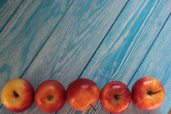 Red apples lie on blue wooden background.
