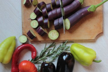 Tahta tahta üzerinde patlıcan daireler kesilmiş, biber ve domates masada.
