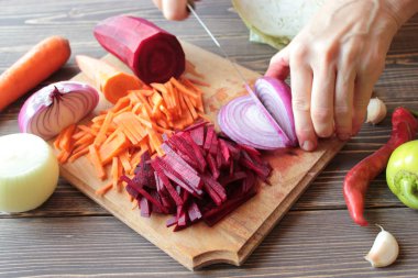 Bir bıçak ile Eller, kesilmiş soğan, pancar ve havuç ahşap bir tahta üzerinde.