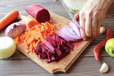 Bir bıçak ile Eller, kesilmiş soğan, pancar ve havuç ahşap bir tahta üzerinde.