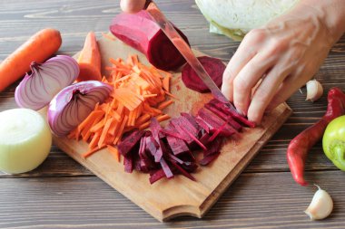 Bir bıçak ile Eller, kesilmiş soğan, pancar ve havuç ahşap bir tahta üzerinde.