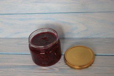 Mavi ahşap arka planda bir kavanoz ahududu reçeli.