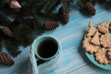 Mavi bir arka plan üzerinde koniler, kurabiye ve çay bardağı ile Köknar dalları.