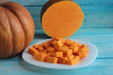 Kabak ve kesilmiş kabak parçaları mavi ahşap arka plan üzerinde beyaz bir tabak üzerinde yatıyor.