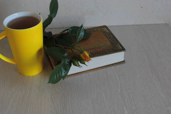 Yellow rose, tea and a book on the table.