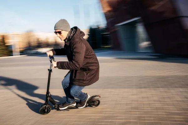 Genç adam rahat kıyafet çekimde caddenin üzerinde elektrik tekme scooter üzerinde bulanıklık sonbaharda