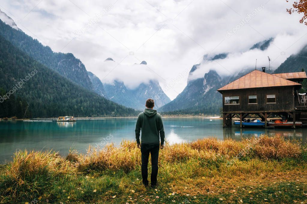 Young man stands back to camera on shore of Dobbiaco Lake or Toblacher in Italy