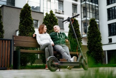 Çiftler sokakta elektrikli scooter 'ın yanına oturur ve gülerler..