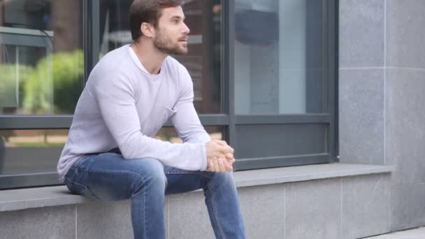 Hombre guapo serio sentado fuera de la oficina y mirando a su alrededor — Vídeo de stock