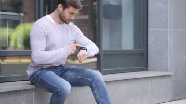 Przystojny mężczyzna siedzący poza godzinami do przeglądania za pomocą zegarka Smartwatch — Wideo stockowe