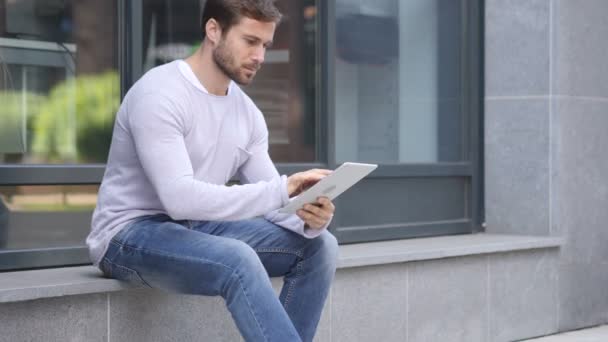 Красивий чоловік за допомогою планшетного ПК під час сидять за межами офісу, перегляду онлайн — стокове відео