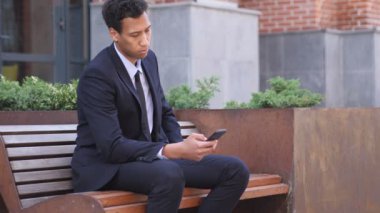 Afrika işadamı kullanarak bankta otururken Smartphone