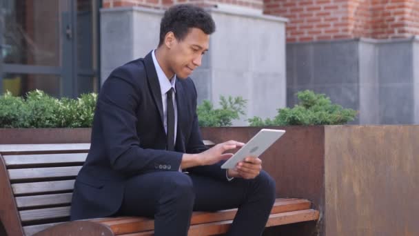 Aufgeregter afrikanischer Geschäftsmann feiert Erfolg auf Tablet im Sitzen — Stockvideo