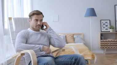 Yetişkin adam konuşurken telefonu dinlenirken sandalye üzerinde iken