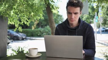 Genç adam içme kahve Cafe Teras içinde Laptop üzerinde çalışırken