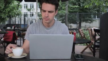 Adam kahve içme ve Cafe Teras otururken dizüstü bilgisayar üzerinde çalışan