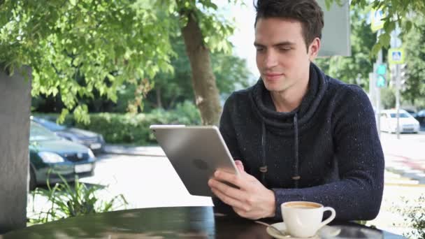 Молодой человек просматривает на планшете, сидя в кафе терраса — стоковое видео