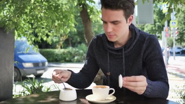 Jeune homme mélangeant sucre et café, assis sur la terrasse du café — Video