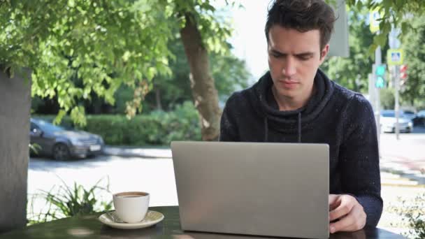 Hombre joven escribiendo en el ordenador portátil mientras está sentado en Café Terraza — Vídeo de stock