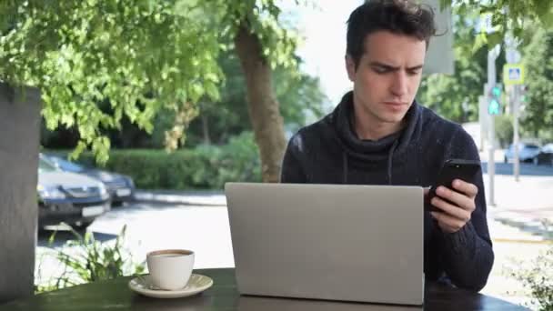 Hombre usando Smartphone mientras trabaja en el ordenador portátil, información — Vídeo de stock