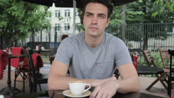 Joven sentado en Café Terraza y mirando a su alrededor — Vídeo de stock