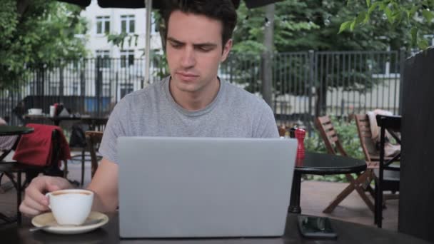 Mann trinkt Kaffee und arbeitet am Laptop, während er auf der Caféterrasse sitzt — Stockvideo