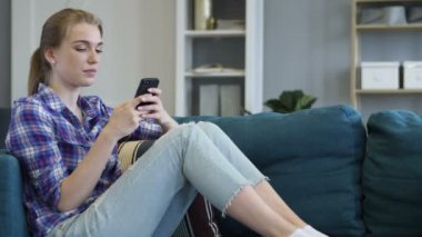 Genç kadın kullanarak akıllı telefon kanepede dinlenirken yaparken