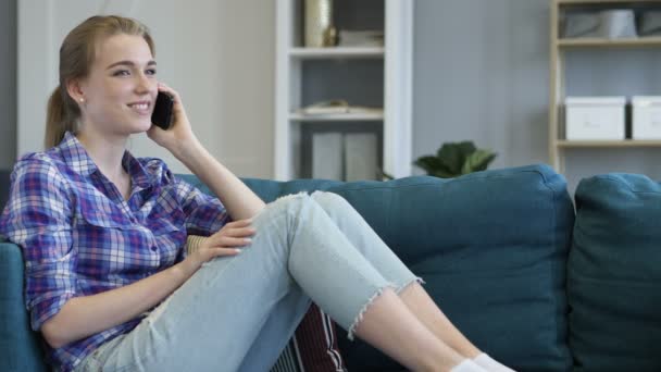 若い女性は、ソファでリラックスしながら電話で話しています。 — ストック動画